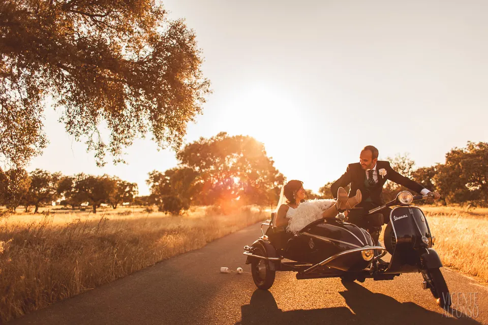 Los novios en una Vespa con sidecar al atardecer, por un camino de campo