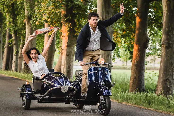 Novios recorriendo un camino arbolado en una Vespa con sidecar