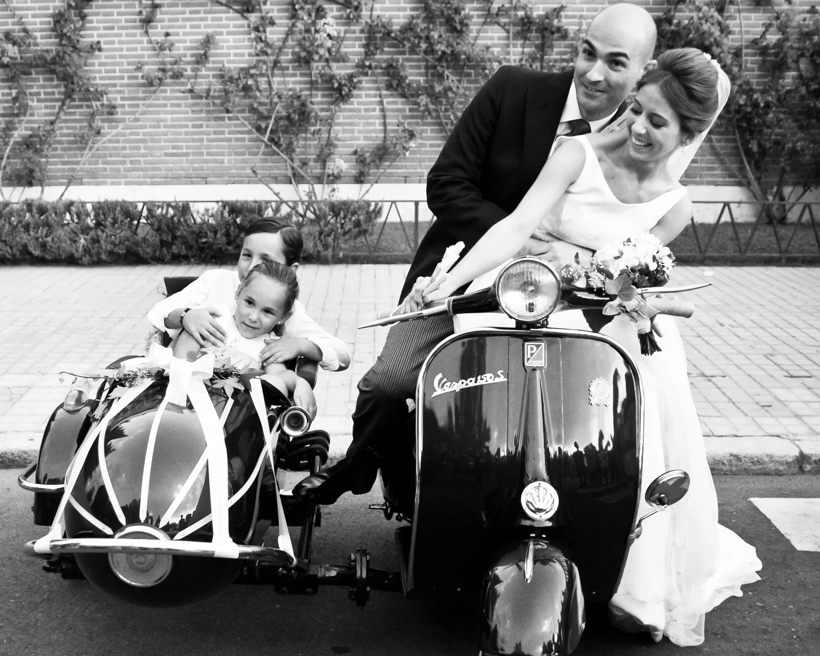Retrato en blanco y negro de los novios junto a una Vespa con sidecar