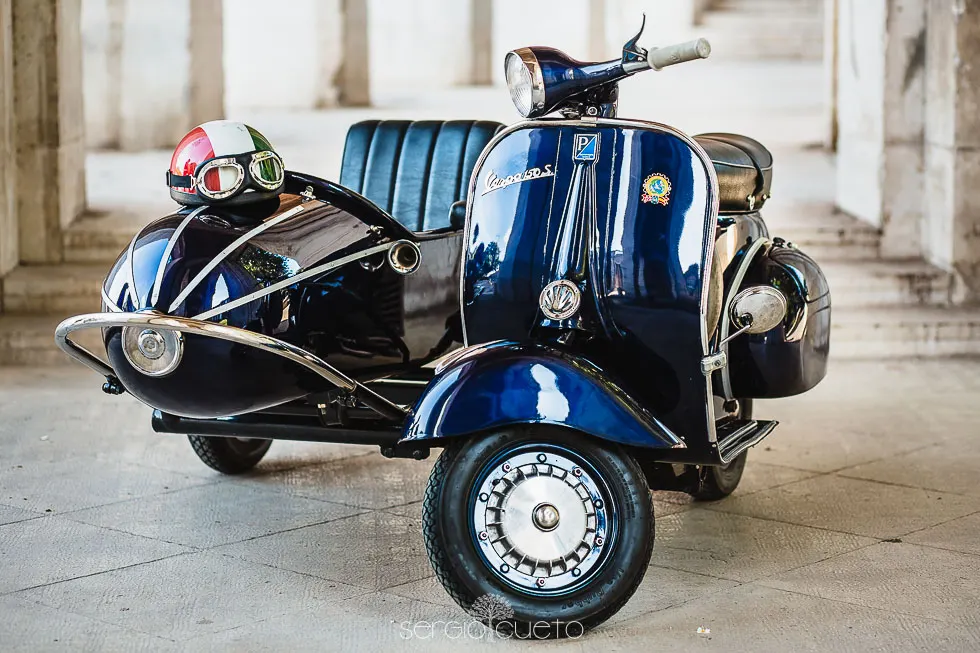 Vespa azul con sidecar clásico bajo una arcada