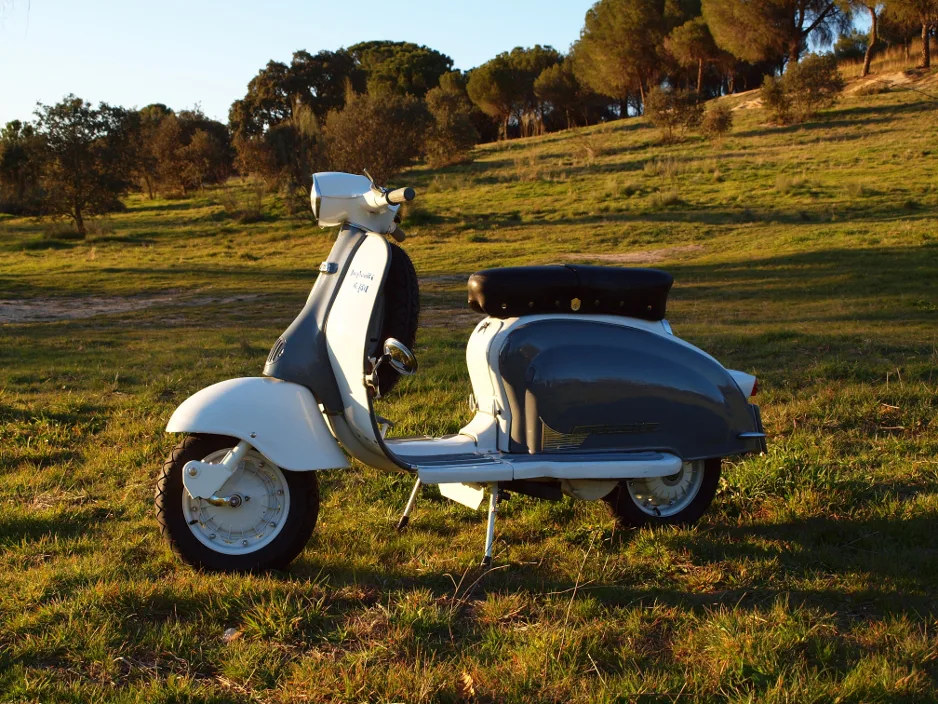 Vespa clásica clara aparcada en un campo al atardecer