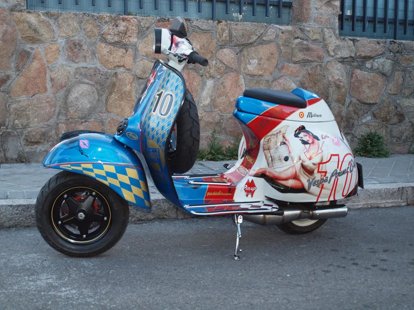 Vespa con decoración gráfica de colores ante un muro de piedra