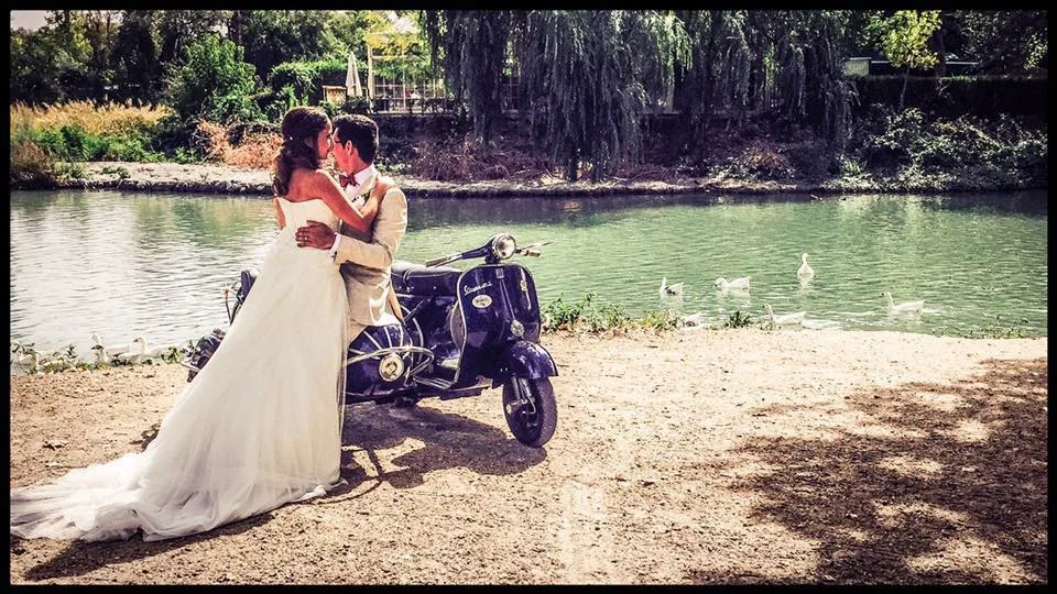 Pareja junto a una Vespa al borde de un lago