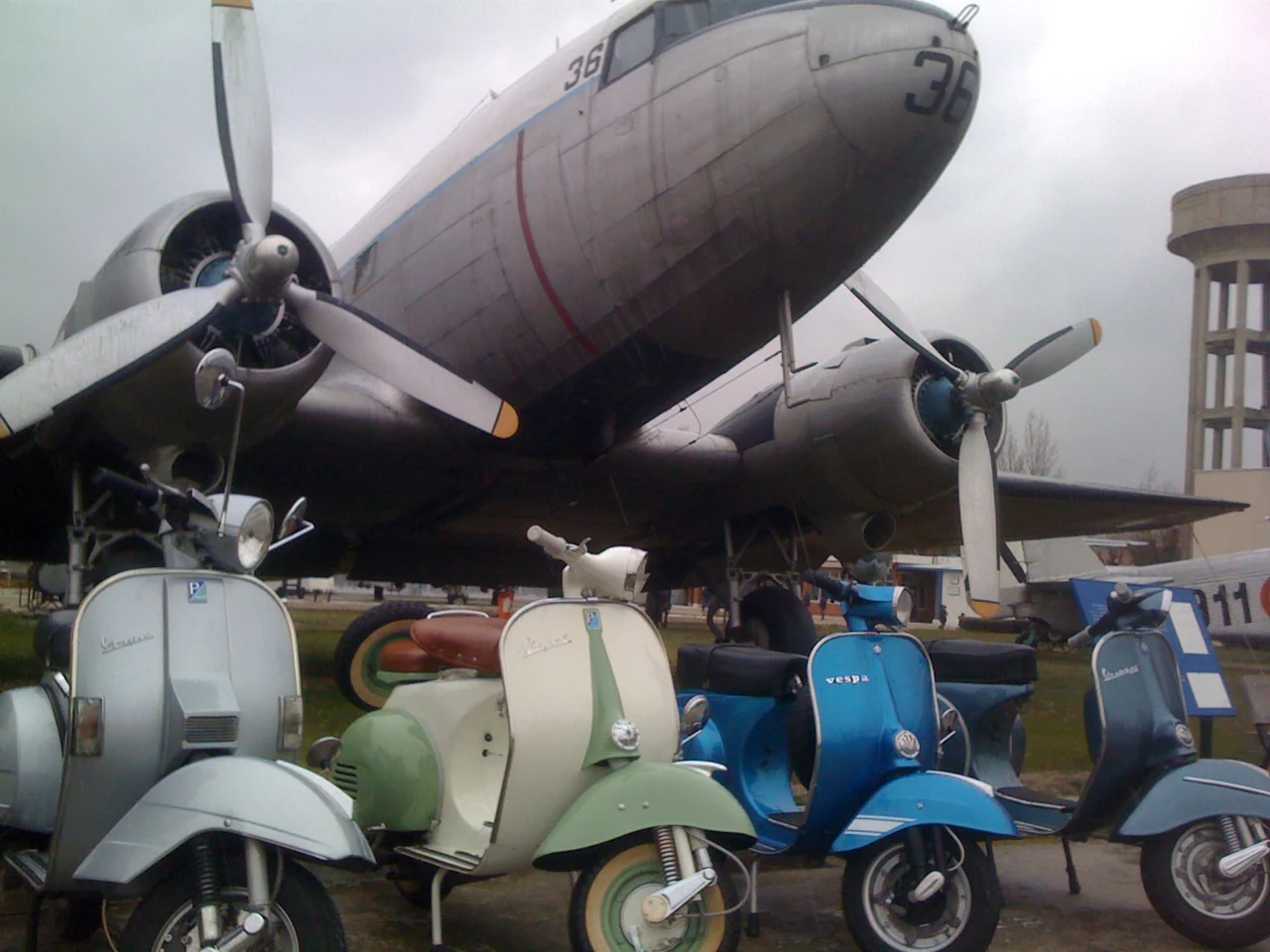 Varias Vespas clásicas expuestas junto a una avioneta